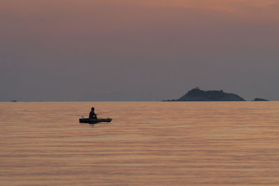 Man on boat at sea against sky during sunset