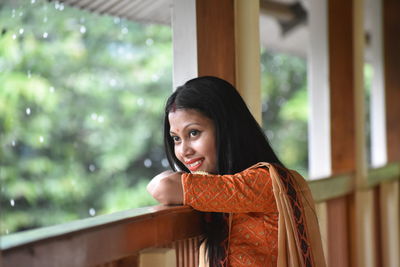 Portrait of smiling young woman against window