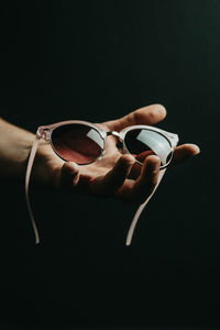 Hand of person holding sunglasses against black background