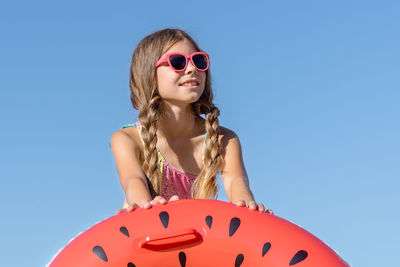 A girl in a swimsuit and glasses plays on the beach with an inflatable ring.