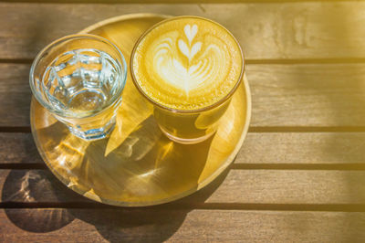 Coffee cup with glass of water on wooden plate wood table., high angle view of coffee on table.