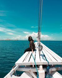 Rear view of man sitting on boat in sea against sky