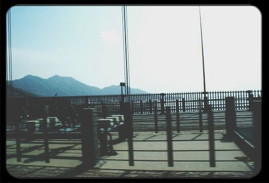 transfer print, mountain, auto post production filter, sky, railing, mountain range, sunlight, window, indoors, built structure, transportation, day, fence, architecture, nature, clear sky, shadow, no people, cloud