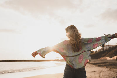 Rear view of woman with arms raised against sky