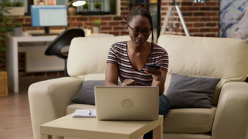 Woman using laptop while sitting on sofa at home