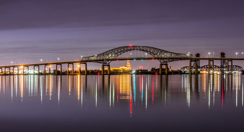 Illuminated bridge over sea against sky at night