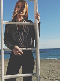 Woman standing by ladder at beach against sky