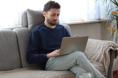 Young man using mobile phone while sitting on sofa