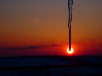 Close-up of icicles against orange sky during sunset