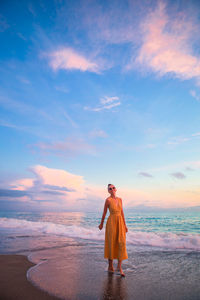 Woman standing on beach against sky during sunset