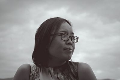 Low angle view of young woman wearing eyeglasses against sky