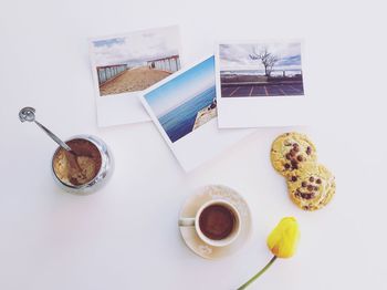 Directly above shot of coffee with flower bud by cookies and photographs on table