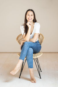 Portrait of young woman sitting on chair against wall