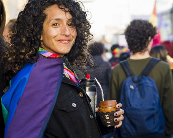 Woman looking at camera while holding a mate with a rainbow flag in an lgbtq pride march.