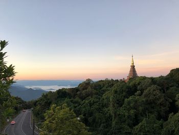 Trees by building against sky during sunset