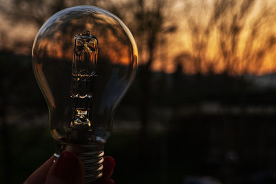 Close-up of hand holding glass against sky during sunset