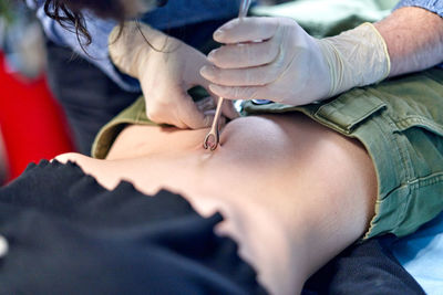 Anonymous body modification artist in glass pinching belly button of female client during piercing procedure in salon