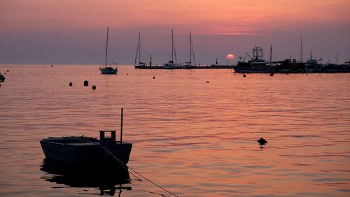 Sailboats moored in sea against sky during sunset