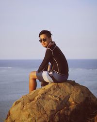 Young woman standing on rock at sea shore against clear sky