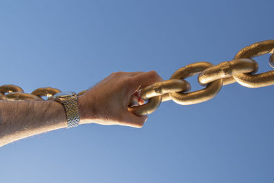 Low angle view of hand holding chain against blue sky