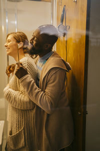 Side view of happy multiracial couple brushing teeth in bathroom at home