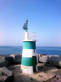 Lighthouse by sea against clear blue sky