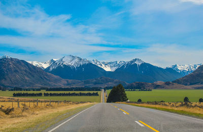 Country road leading towards mountains against sky