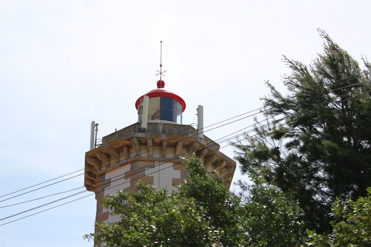 LOW ANGLE VIEW OF LIGHTHOUSE AMIDST TREES AND BUILDINGS AGAINST SKY