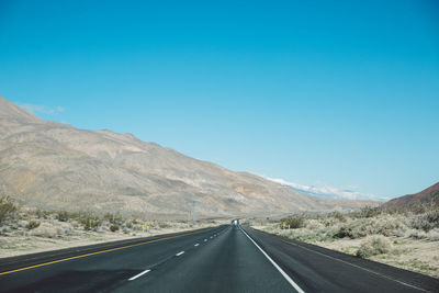 Empty road by mountains against clear blue sky