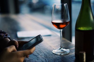 Cropped hand of woman using mobile phone by red wine on table