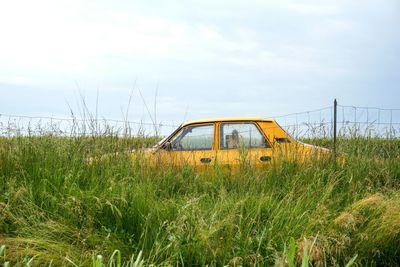 Scenic view of car parked in grass area against cloudy sky