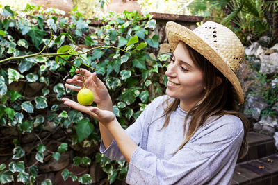 Smiling woman picking lemon from plant