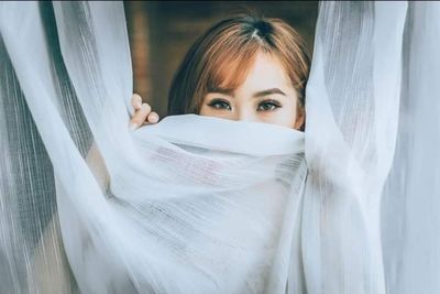 Portrait of young woman hiding behind curtain