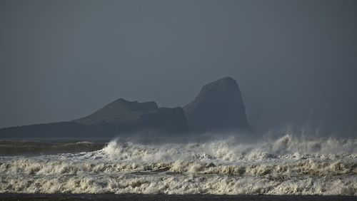 Scenic view of waves crashing against rocks below clear sky