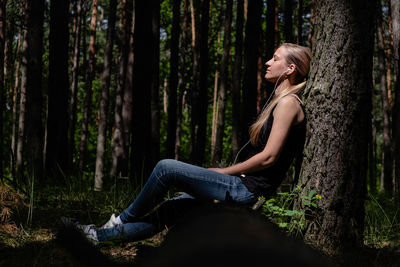Side view of young woman sitting on tree trunk in forest