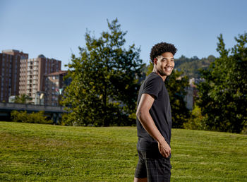 Young man standing on grass against trees