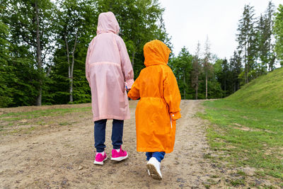 Rear view of boys wearing raincoat while walking on pathway in forest