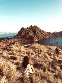 Rear view of woman sitting on beach against clear blue sky