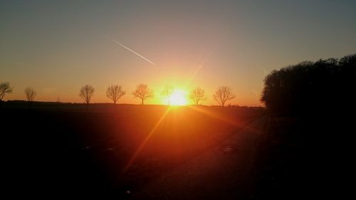 Silhouette trees on landscape against sunset sky