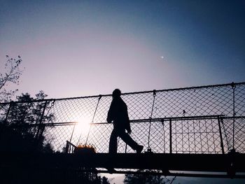 Low angle view of silhouette man walking on footbridge against sky