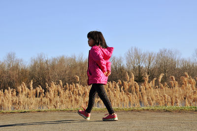 Side view of girl in pink cloth by reeds against sky