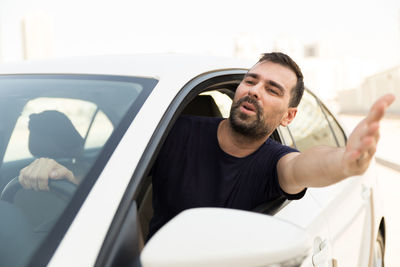 Frustrated man gesturing through window while traveling in car