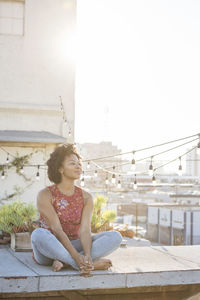 Young woman sitting on rooftop terrace, enjoying the sun