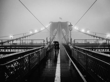 Rear view of couple walking on brooklyn bridge during rain