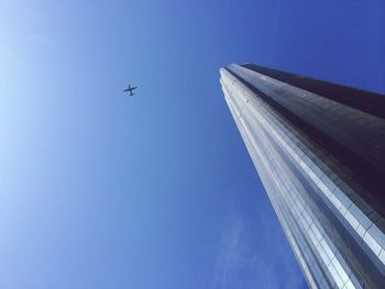 Low angle view of world trade center against airplane flying in blue sky