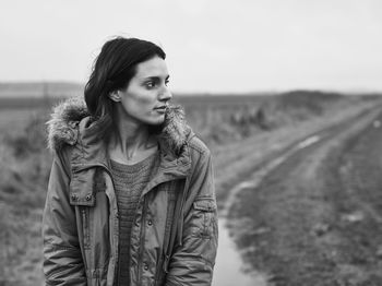 Portrait of beautiful young woman standing on road against sky