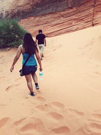 Full length rear view of people walking on sandy field against rock at moapa valley