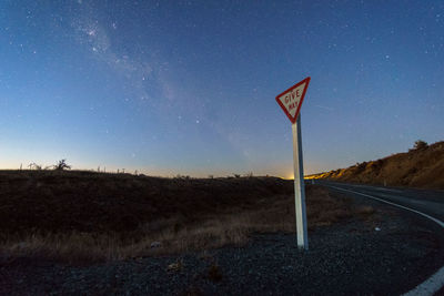 Road sign on field against clear sky at night
