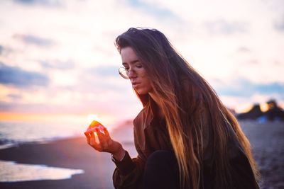 Young woman holding seashell at beach during sunset