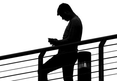 Side view of man looking at railing against clear sky
